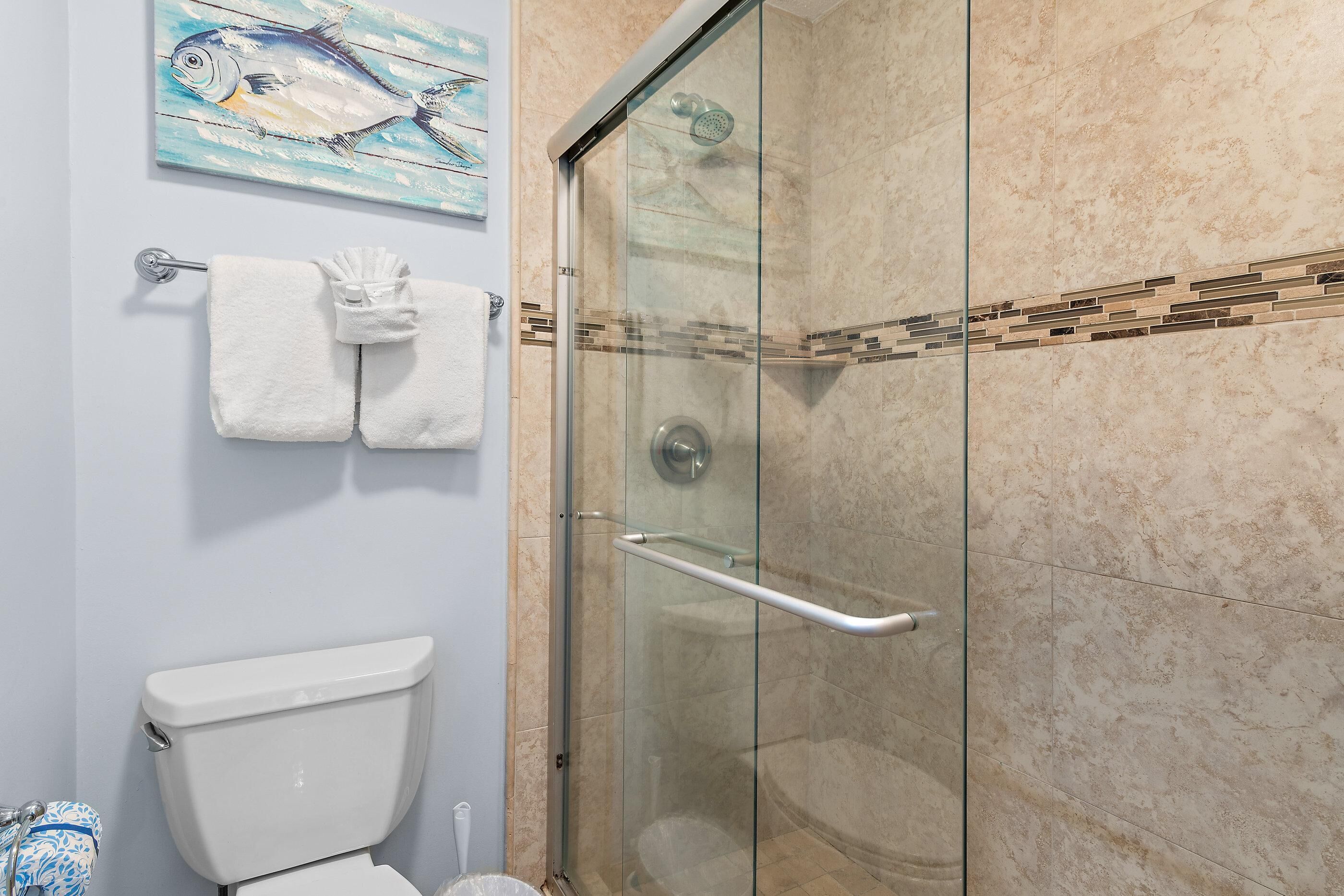 A bathroom with a glass-enclosed shower, a toilet, and a towel rack with two white towels.