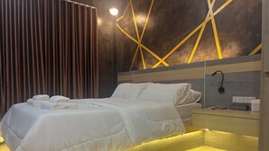 A modern hotel room with a neatly made bed, a bedside table with a lamp, and a wall with geometric patterns. - ที่พัก ใกล้เมืองสุราษฎร์ธานี (Surat Thani)