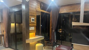 A modern interior with a wooden wall, a seating area with a red ottoman, and a glass partition. - ที่พัก ใกล้เมืองสุราษฎร์ธานี (Surat Thani)