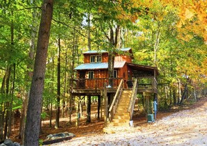 A wooden treehouse with a staircase leading up to it, surrounded by a forest. - Cherry Treesort “Traci’s Treasure” (Rowan County)