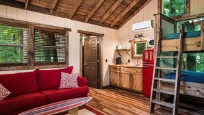 A cozy cabin interior with a red sofa, wooden floors, a kitchen area, and a loft bed with a ladder. - Cherry Treesort "The Tolson" (Rowan County)