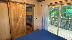 A bedroom with a bed, a wooden door, and a view of a deck. - Cherry Treesort "The Tolson" (Rowan County)