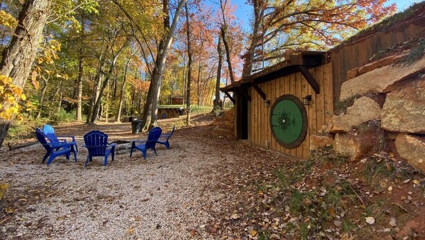 A rustic cabin with a stone exterior and a green door, surrounded by trees with autumn foliage. - Cherry Treesort "Mimi and Papa's" (Rowan County)