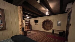 A room with a bed, a wooden bench, a round wooden wall feature, a small table, and a shelf with items. - Cherry Treesort "Mimi and Papa's" (Rowan County)