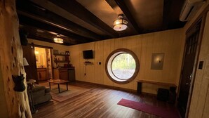 A room with wooden flooring, a round window, a sofa, a coffee table, and a door. - Cherry Treesort "Mimi and Papa's" (Rowan County)
