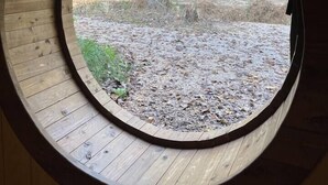 A circular window with a view of a forested area and a dirt path. - Cherry Treesort "Mimi and Papa's" (Rowan County)