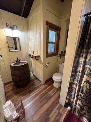 A small, rustic bathroom with wooden walls, a wooden barrel sink, a toilet, and a window. - Cherry Treesort "Chico's Hideaway" (Rowan County)