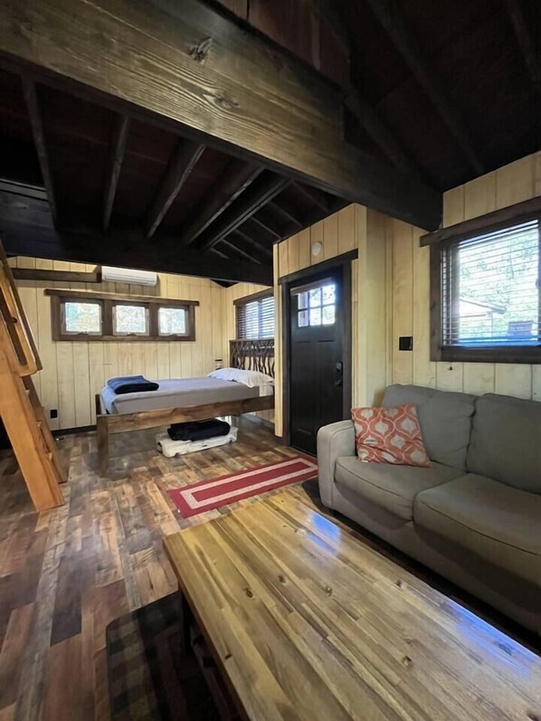 A cozy cabin interior with a wooden floor, a bed, a sofa, and a table.
