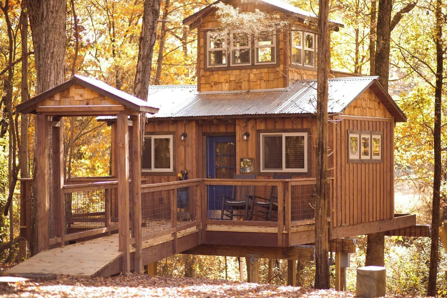 A wooden cabin with a balcony and a small porch, surrounded by trees.