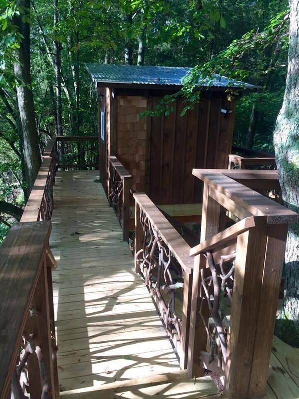 Une terrasse en bois avec des bancs et une petite construction en bois, située dans une zone boisée.
