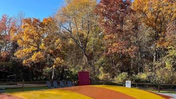 A playground with a yellow and orange surface, surrounded by trees with autumn foliage.