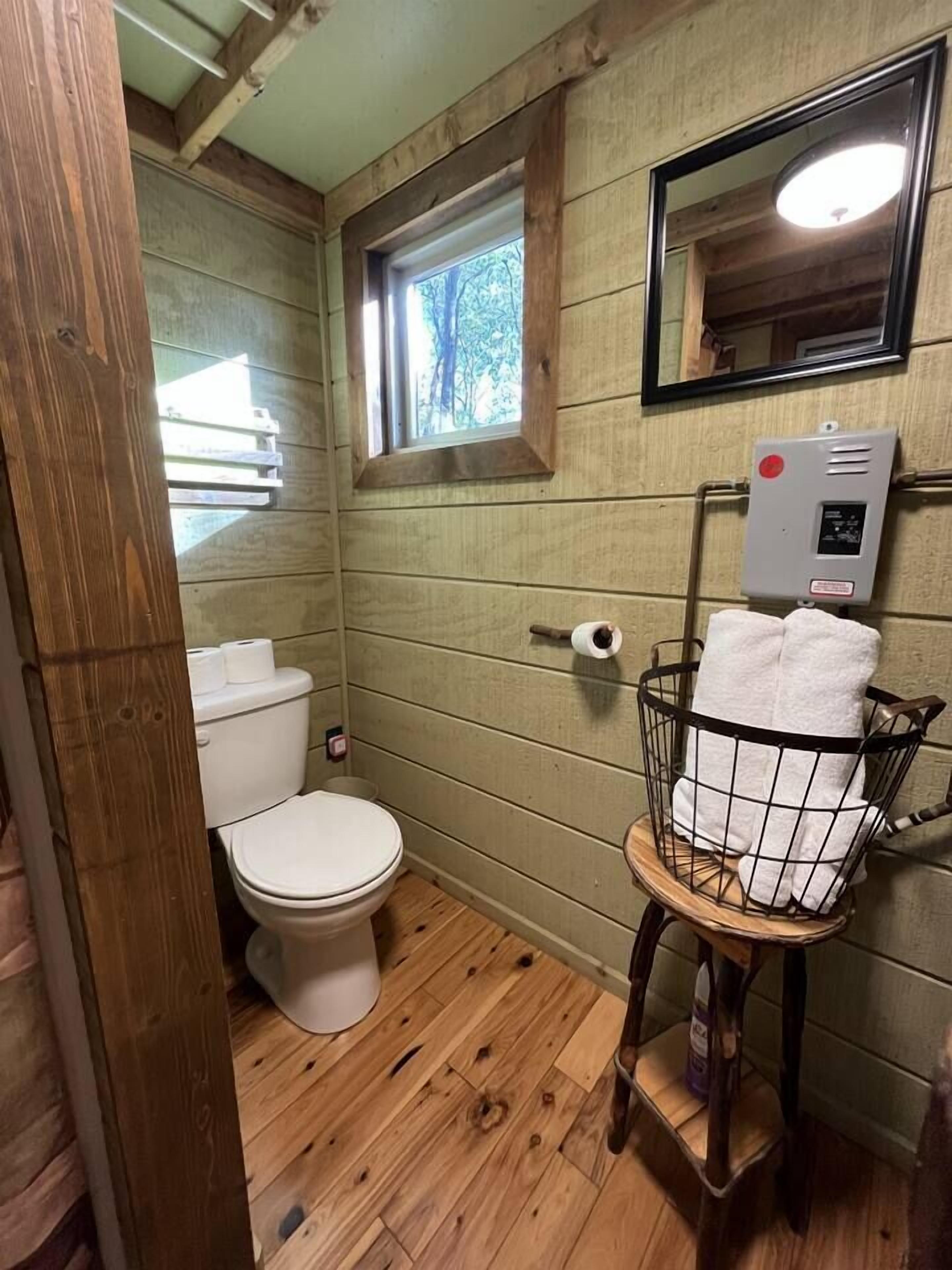 Un baño pequeño y rústico con paredes de madera, un inodoro, una ventana y un perchero con una cesta.