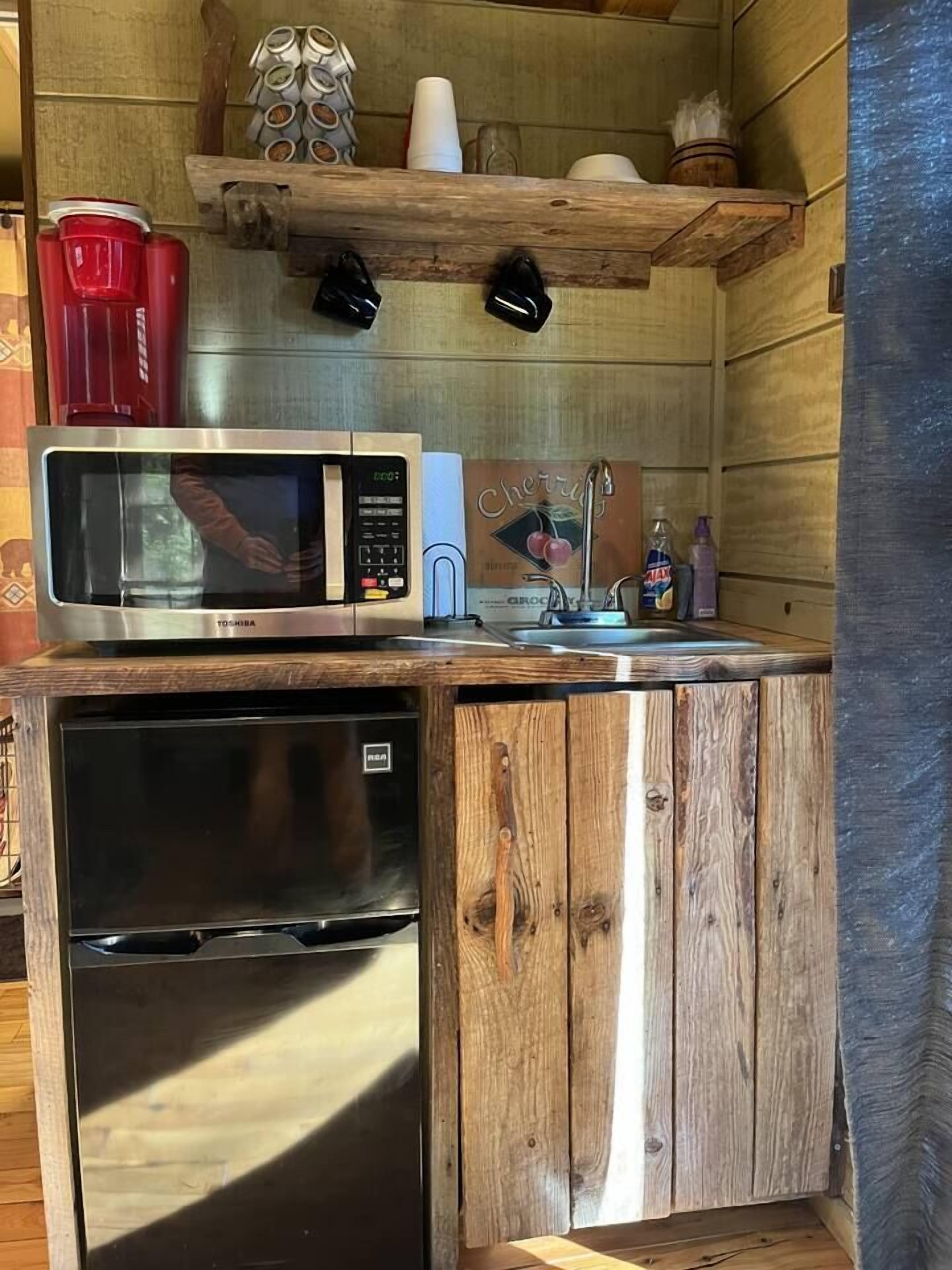 A compact kitchen with a microwave, refrigerator, and wooden cabinets.