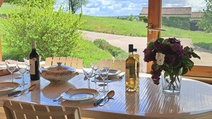 A dining table set for six with wine bottles, glasses, and a vase of flowers, overlooking a green landscape.