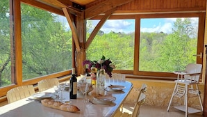 A dining area with a long table set for six, large windows, and a view of a forest.