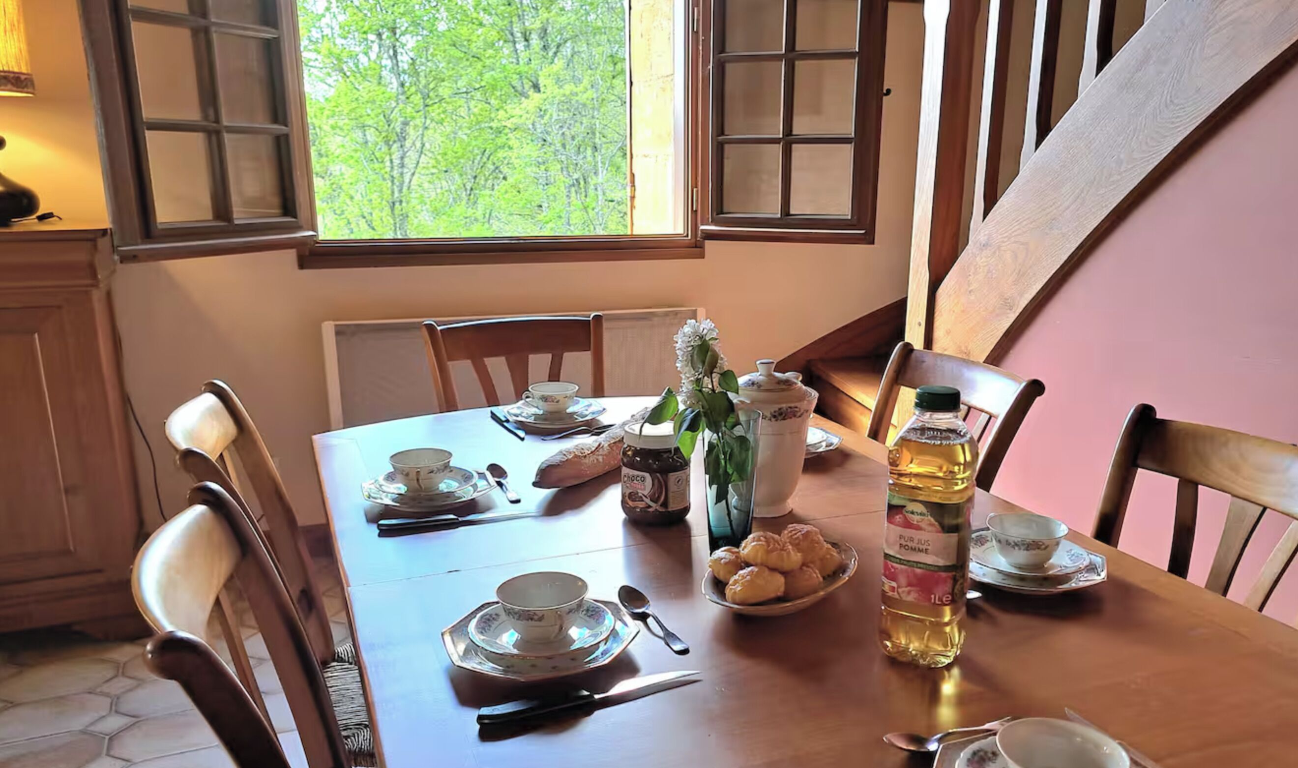 Une table à manger dressée avec des assiettes, des tasses, une bouteille de jus de fruits et des pâtisseries.