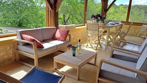 An outdoor patio with wooden furniture, including a sofa, chairs, and a table.