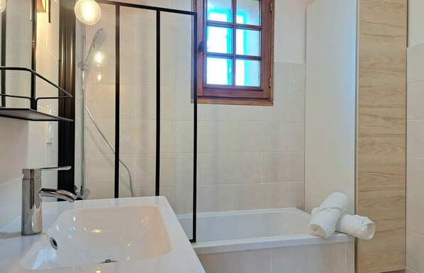Un baño moderno con un lavamanos blanco, una bañera y una ventana con marco de madera.