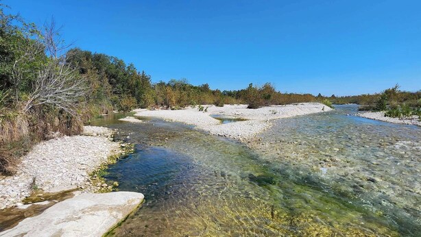A clear river with rocky banks and sparse vegetation.