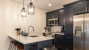 A modern kitchen with dark cabinets, stainless steel appliances, a white island with stools, and pendant lighting.