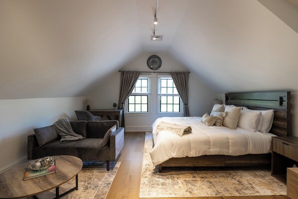 A bedroom with a large bed, a sofa, a small table, and a window with curtains.