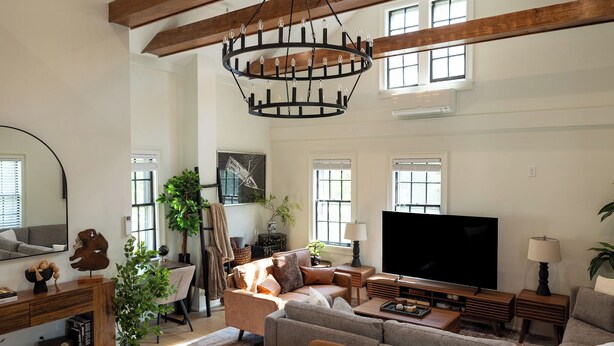 A spacious living room with a large TV, comfortable seating, and a modern chandelier.