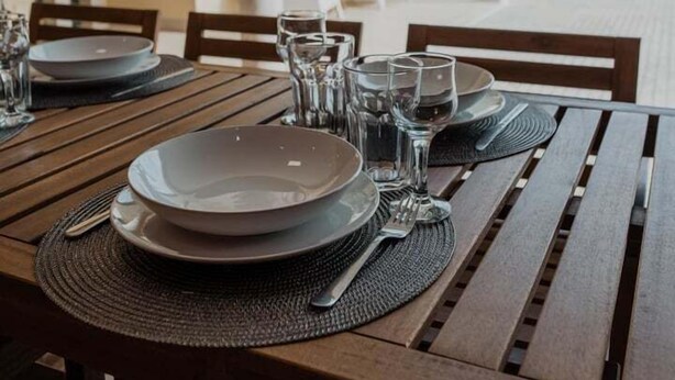Een eettafel buiten gedekt met borden, glazen en bestek.