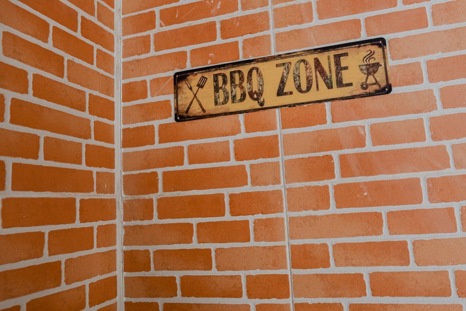 Un mur de briques sur lequel est affiché un panneau indiquant « Zone barbecue ».