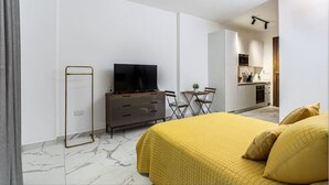 A modern hotel room with a bed, a TV, a small dining table, and a kitchenette. - Luxurious Studio close to USA embassy (Accra)