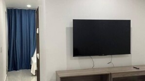 A modern hotel room with a flat-screen TV mounted on the wall, a wooden console table, and a bench. - D&X Apartment-H | 2-Bed, Kitchen, AC, WiFi, TV (Kralendijk)