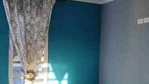 A room with a ceiling fan, a sofa with colorful pillows, a patterned curtain, and a window with sunlight casting shadows.
