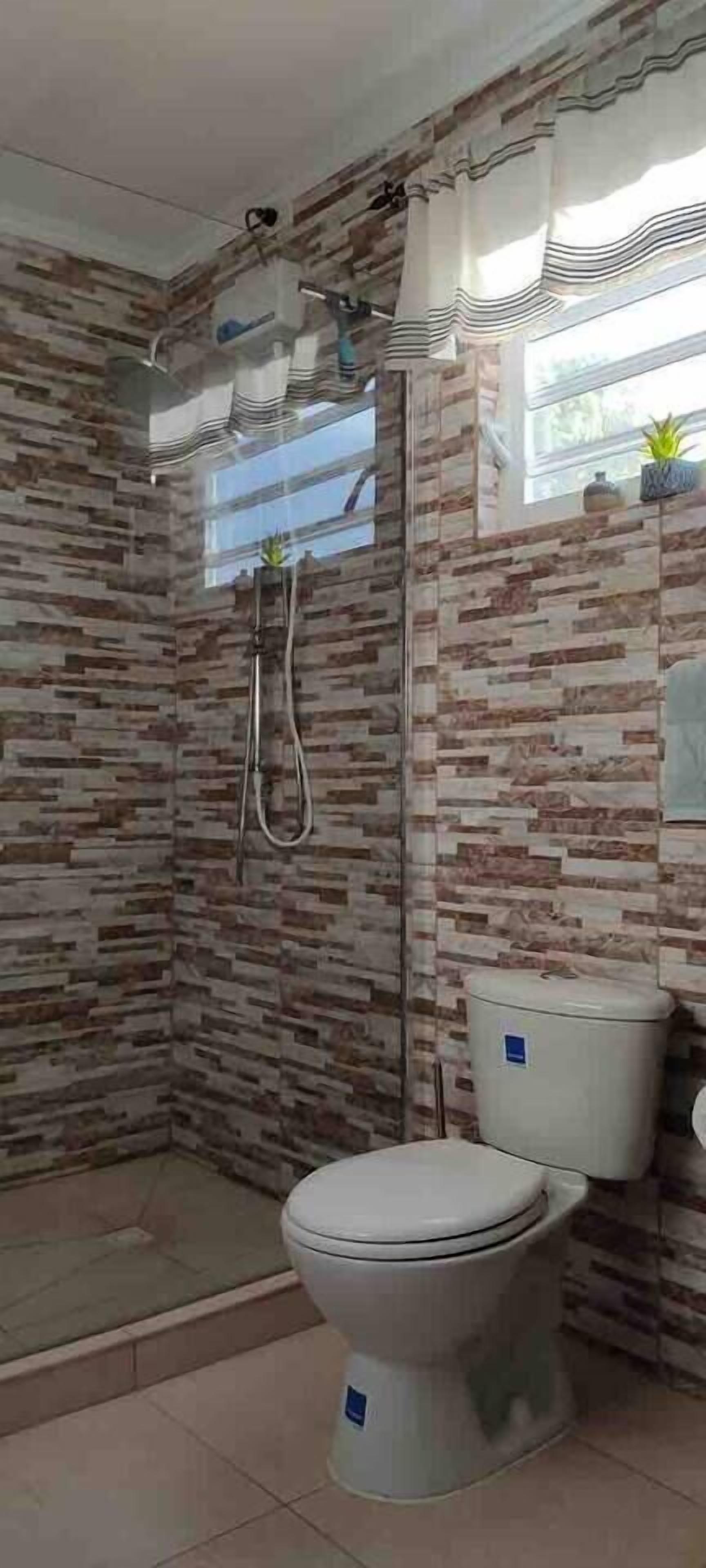 A bathroom with a shower, toilet, and a window with curtains.