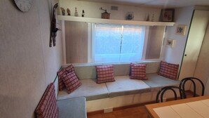 A cozy room with a built-in bench, a clock on the wall, and a window with curtains. - MOBIL HOME LOUPIOTS 4/6 PERS. (Besse-et-Saint-Anastaise)