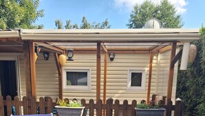 A covered outdoor area with two blue lounge chairs, a barbecue grill, and a wooden fence. - MOBIL HOME LOUPIOTS 4/6 PERS. (Besse-et-Saint-Anastaise)