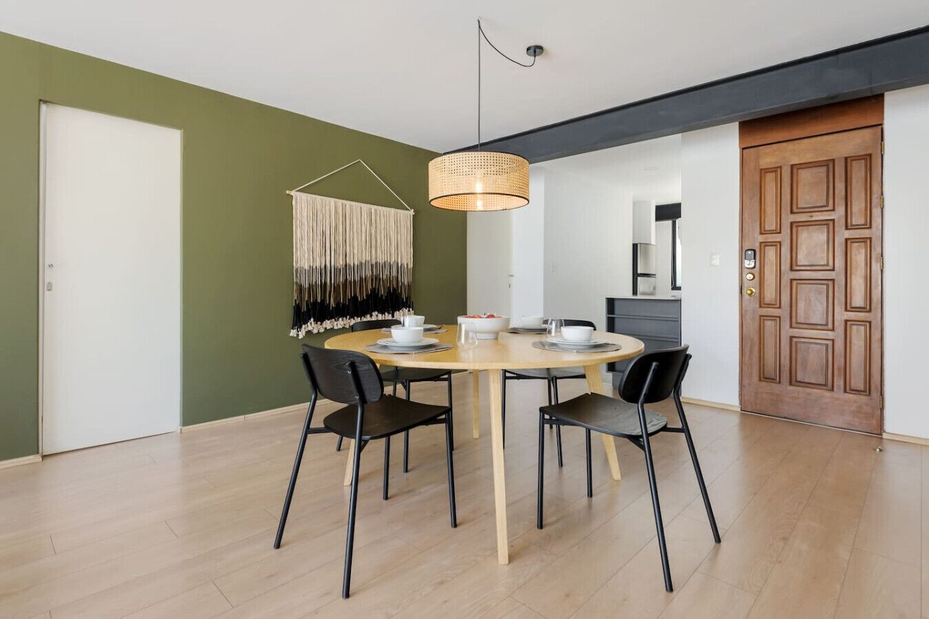 A dining area with a round table, four chairs, a hanging light fixture, and a wall-mounted macrame piece.
