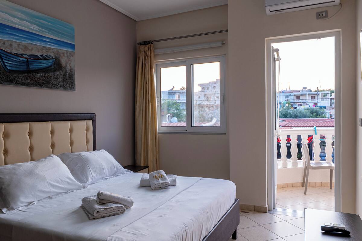 A hotel room with a bed, a painting, a window, and a balcony.