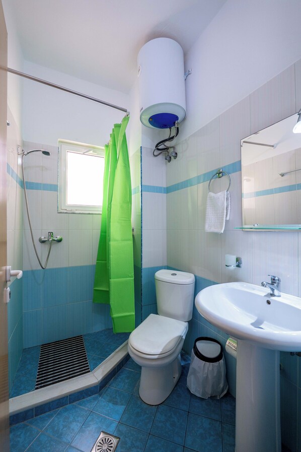 A bathroom with a shower, toilet, sink, and a window with a curtain.