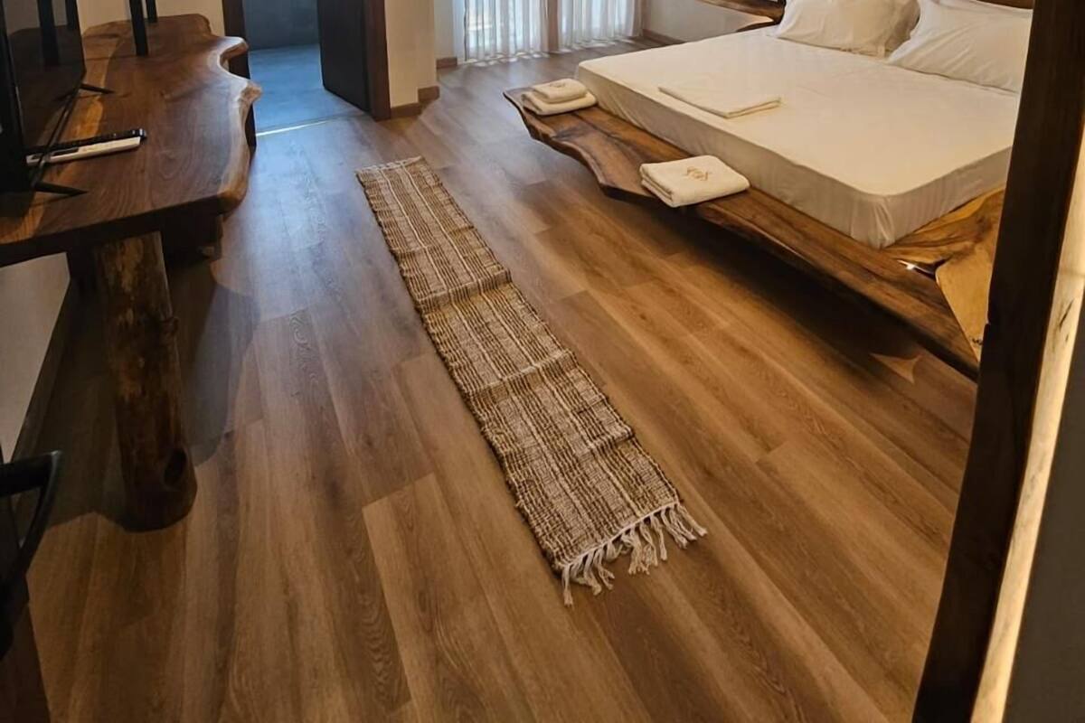 A modern bedroom with a wooden bed frame, a desk, and a large window with curtains.