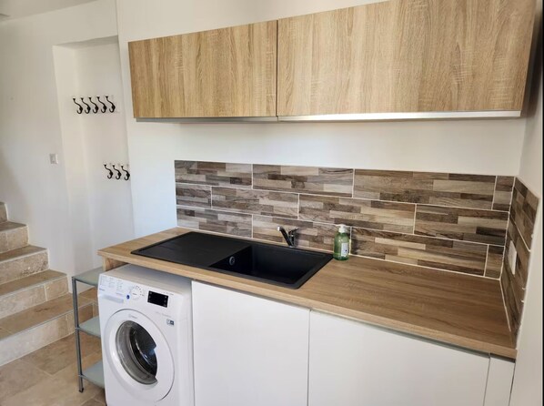 A compact kitchen with wooden cabinets, a built-in sink, and a front-loading washing machine. - Guest House in Allauch (Allauch)