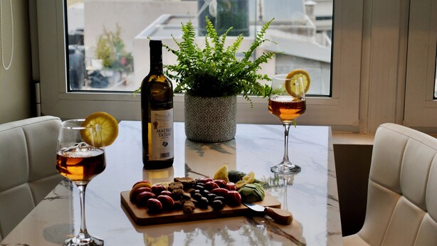 A dining table with a bottle of wine, two glasses of wine, a fruit platter, and a potted plant.