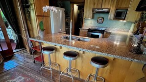 A kitchen with wooden cabinets, a granite countertop, and a bar area with stools. - Delightful retreat Log Home in Horseshoe Bend, ID (Horseshoe Bend)