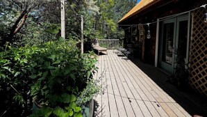 A wooden deck with potted plants, a lounge chair, and a building with a wooden facade and a tower. - Delightful retreat Log Home in Horseshoe Bend, ID (Horseshoe Bend)