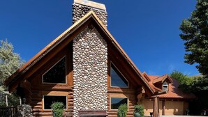 A log cabin with a stone chimney, large windows, and a garage. - Delightful retreat Log Home in Horseshoe Bend, ID (Horseshoe Bend)