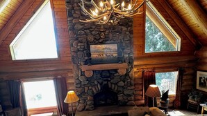 A log cabin interior with a stone fireplace, wooden beams, and a chandelier. - Delightful retreat Log Home in Horseshoe Bend, ID (Horseshoe Bend)
