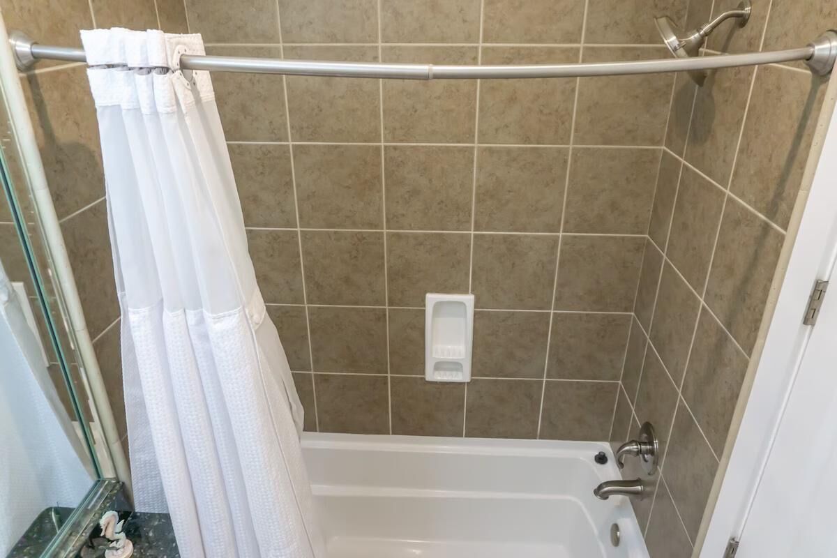 Eine Dusche mit weißer Duschkabine, einer Handbrause und einem Seifenspender an der Wand.