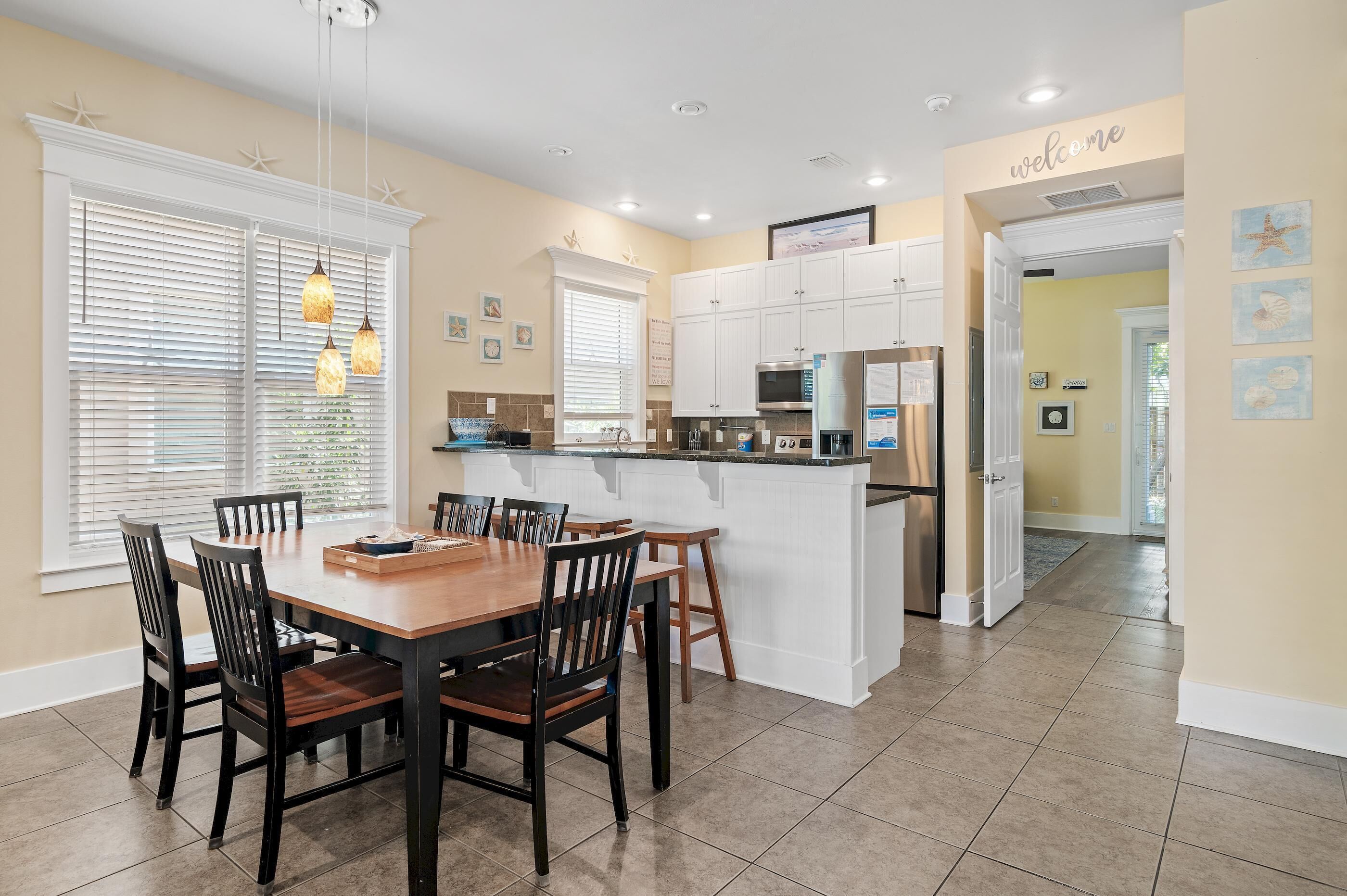 A modern kitchen with white cabinets, a central island, and a dining area with wooden chairs.