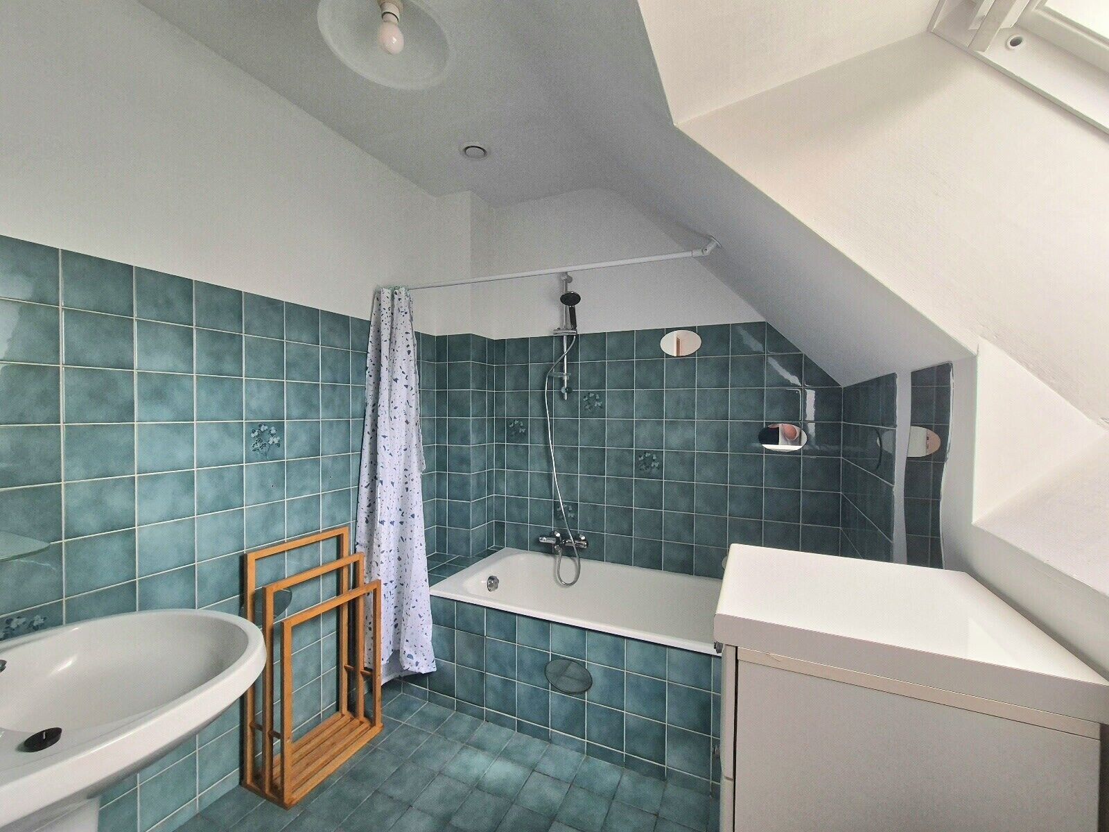 Une salle de bain équipée d’une baignoire, d’une douche et d’un lavabo, avec des carreaux bleus et un plafond en pente.