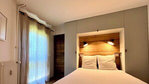 Een slaapkamer met een bed, een houten hoofdbord, een radiator en een raam met gordijnen.