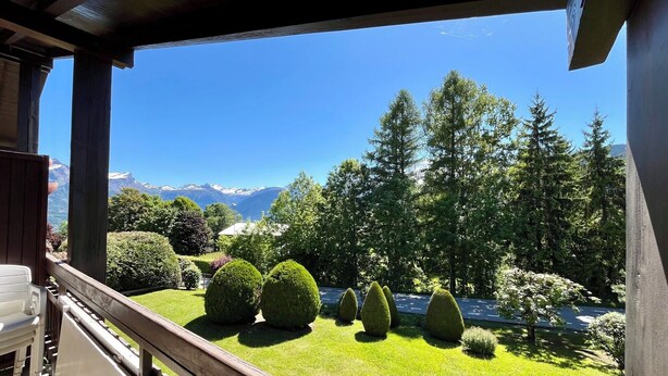 Ein Balkon mit Blick auf einen gepflegten Garten, Bäume und entfernte Berge.