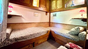 Ein gemütliches Blockhauskabinenzimmer mit Holzwänden, zwei Betten mit gemusterten Bettbezügen und kleinen Nachttischen mit Lampen.